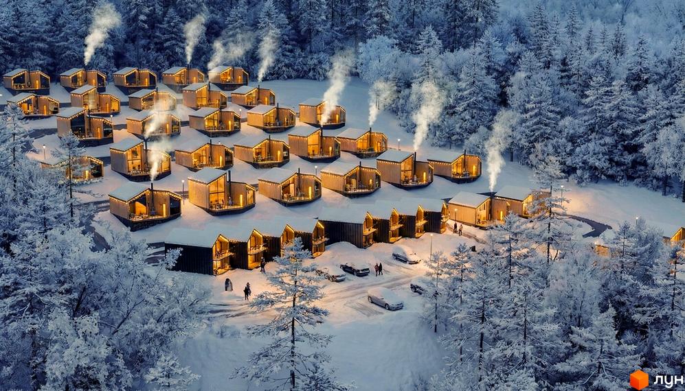 Котеджне містечко Теплий: дерев'яні будинки з панорамними вікнами в засніженому лісі, дим з труб, освітлені вікна, автомобілі на території.