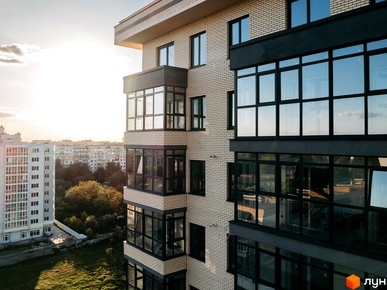 Житловий комплекс Династія: багатоповерховий будинок з цегляним фасадом, заскленими балконами та темними віконними рамами. Навколо зелена територія.