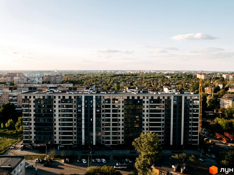 Житловий комплекс Династія - багатоповерховий будинок з темними та світлими фасадами, великою кількістю вікон та балконів. На прибудинковій території розташовані автомобілі та дерева.