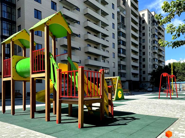 Житловий комплекс Династія: сучасні будинки з балконами та дитячий майданчик з гірками та гойдалками.