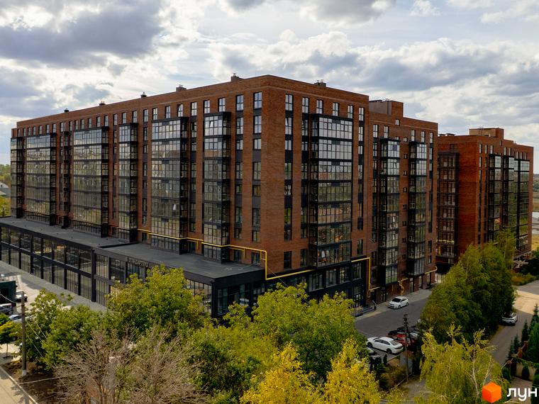 Житловий комплекс Стандарт: цегляна новобудова з панорамним склінням та прибудинковою територією з деревами та автомобілями.