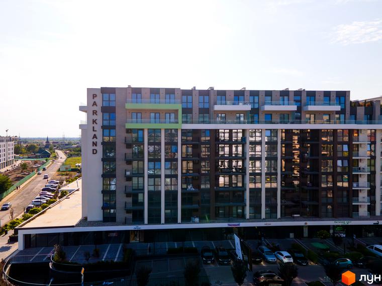Зовнішній вигляд новобудови PARK LAND з балконами та панорамними вікнами, поруч дорога з автомобілями та зелені насадження.