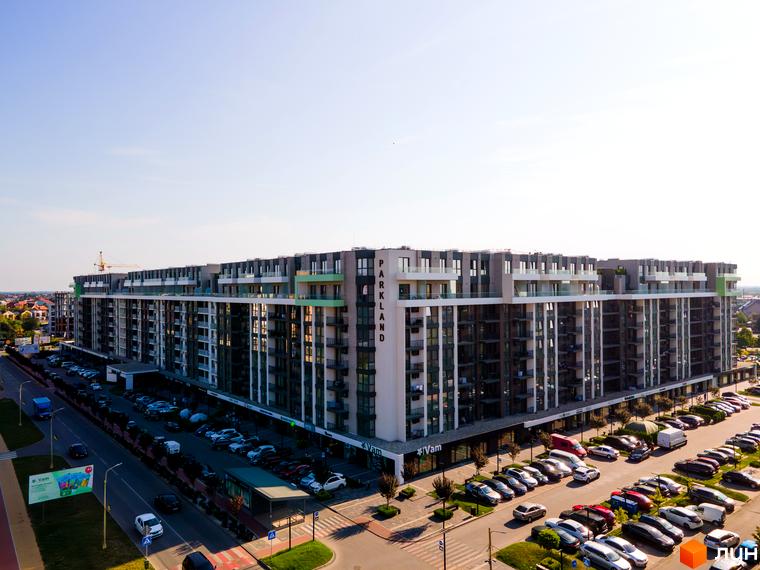 Житловий комплекс PARK LAND: довга багатоповерхова будівля з балконами, сірими та зеленими фасадами. Поруч розташовані парковка та дорога з автомобілями.