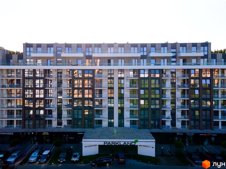 Багатоповерховий будинок Житлового комплексу PARK LAND з балконами та великими вікнами. Перед будинком розташована парковка та комерційні приміщення.