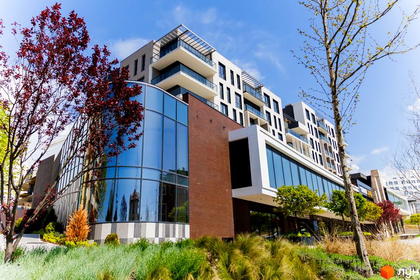 Житловий комплекс Grand Hills: багатоповерховий будинок з фасадами світлих відтінків, великими вікнами та скляними балконами, оточений доглянутим газоном і деревами.