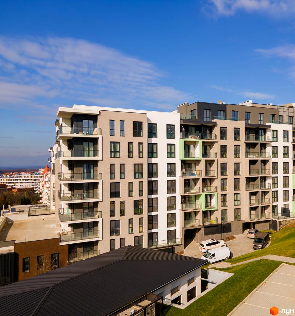 Новобудова Grand Hills зі світло-бежевим фасадом, балконами, скляними огорожами та зеленими газонами.