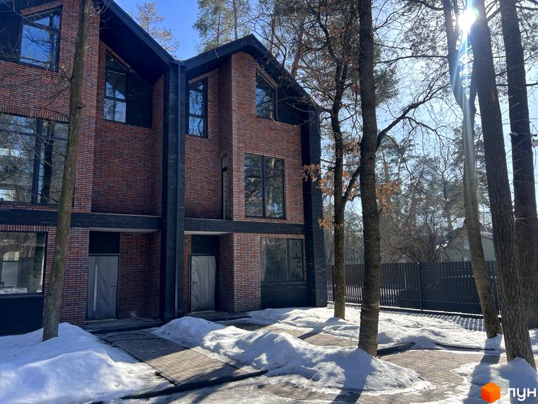 Таунхаус Forest Lane з цегляним фасадом та великими вікнами, розташований серед дерев. Навколо таунхаусу видно доріжки, вкриті плиткою, та сніг.