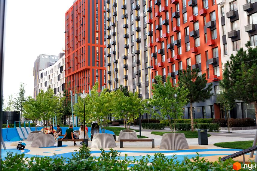 Житловий комплекс Svitlo Park з багатоповерховими будинками в помаранчевих, сірих та білих тонах. На прибудинковій території зелені дерева, лавки та дитячий майданчик.