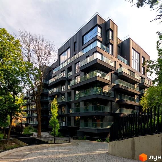 Новобудова Avalon Prime з темним фасадом, скляними балконами та великими вікнами. Навколо багато зелених дерев та брукована доріжка.