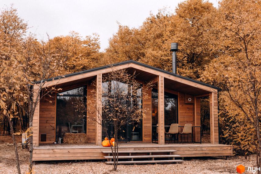 Комплекс відпочинку УЛІС Віняви. Дерев'яний будинок з великими вікнами на тлі осіннього лісу, з терасою та зоною відпочинку.
