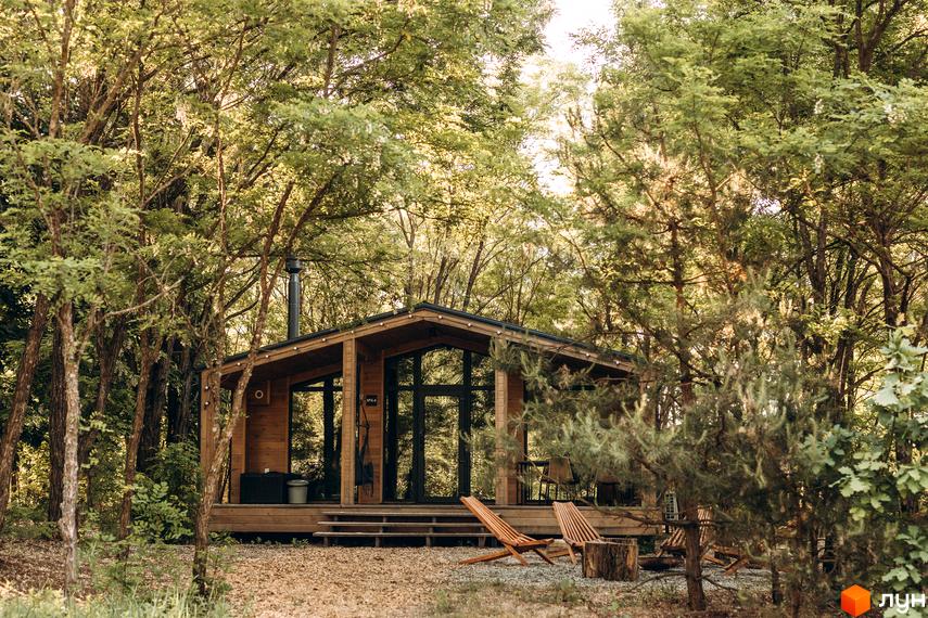 Дерев'яний будинок Комплекс відпочинку УЛІС Віняви з похилим дахом, панорамними вікнами та терасою. Розташований серед густого лісу, з шезлонгами на подвір'ї.