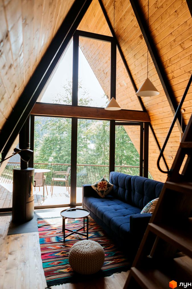 Інтер'єр Котеджного комплексу УЛІС Ворохта: дерев'яні стіни, панорамні вікна з видом на ліс. Синій диван, килим та піч.
