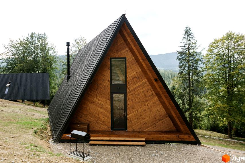 Комплекс відпочинку УЛІС Ворохта: дерев'яна а-подібна будівля з чорною покрівлею та великими вікнами, розташована серед зелених дерев та гір.