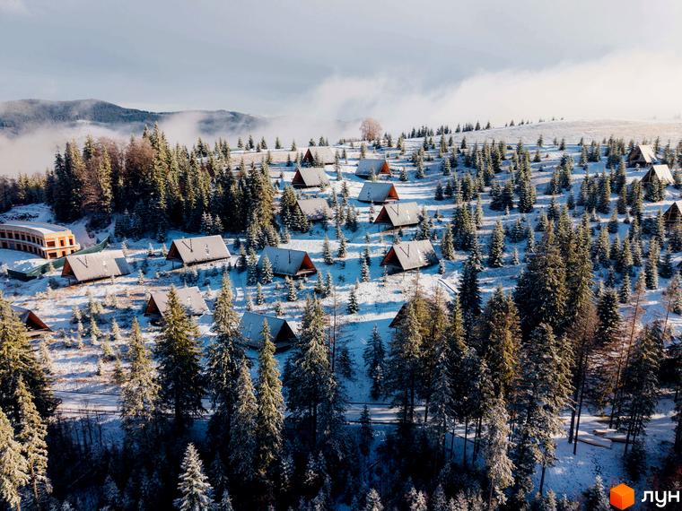 Комплекс відпочинку УЛІС Ворохта - дерев'яні будиночки на сніжному схилі серед ялинок. На території комплексу розташована багатоповерхова будівля.