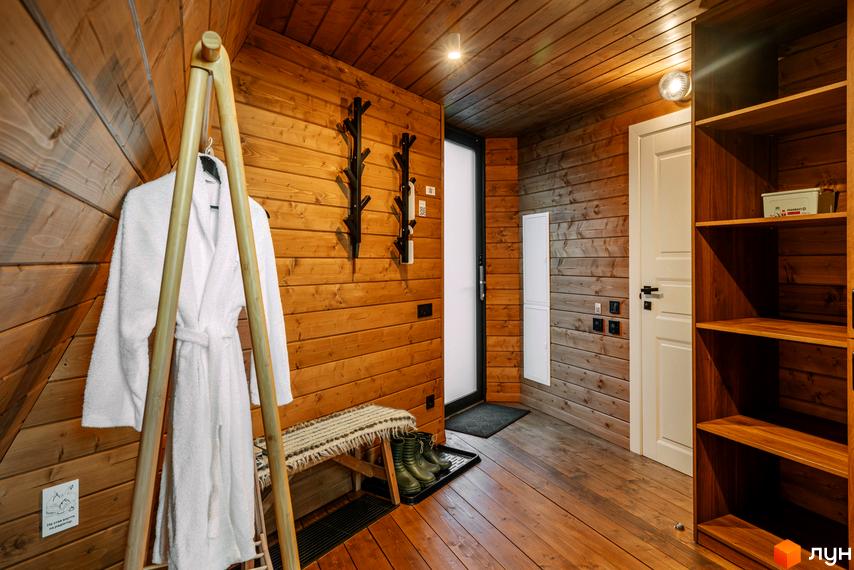 Інтер'єр передпокою в дерев'яному будинку комплексу відпочинку УЛІС Ворохта з халатом, лавкою та полицями.