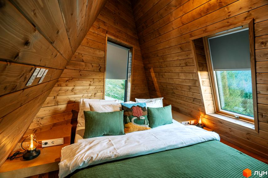 Затишна спальня в дерев'яному будиночку комплексу відпочинку УЛІС Ворохта з двома вікнами та видом на природу.