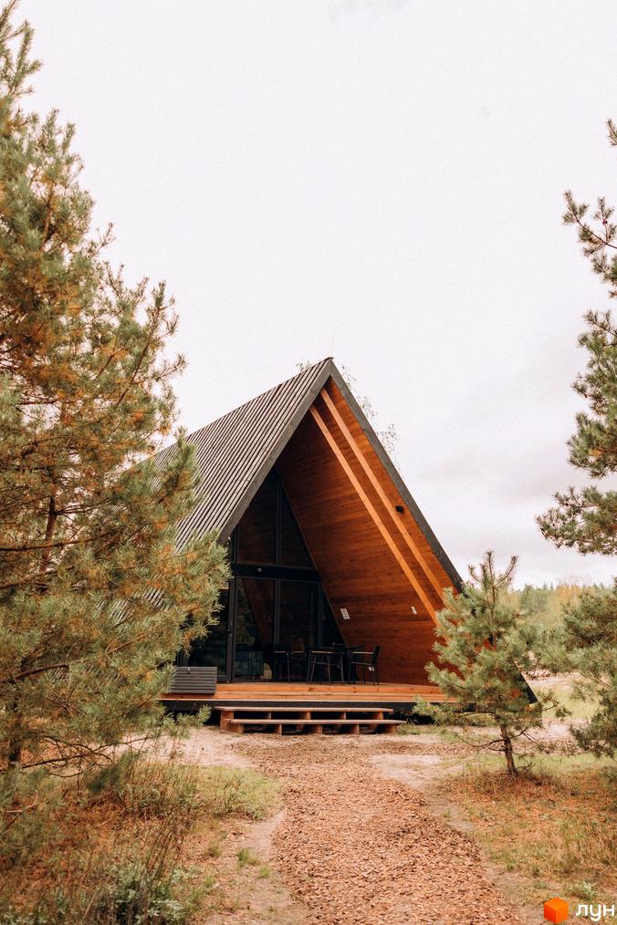 А-подібний дерев'яний будинок в оточенні сосен. Комплекс відпочинку УЛІС Дудки з терасою та зоною відпочинку.