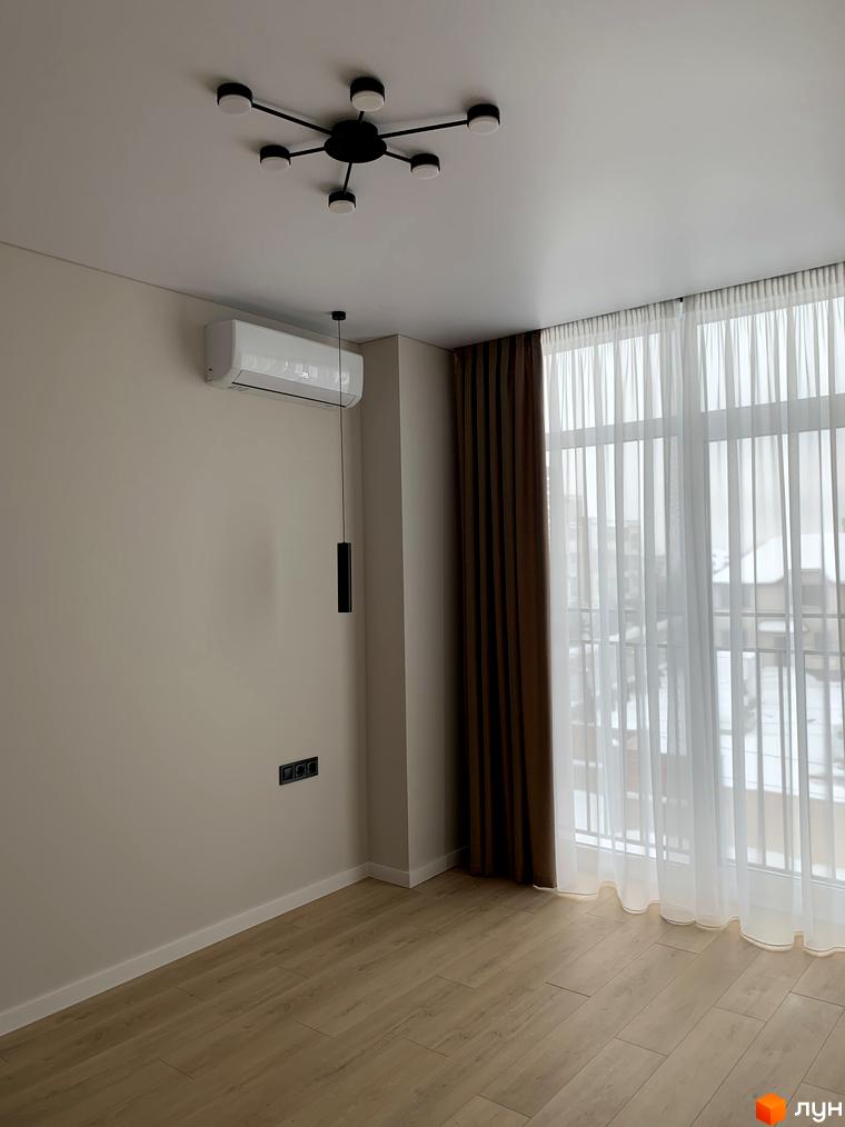 Інтер'єр кімнати в Житловому комплексі Fine Flats: світлі стіни, дерев'яна підлога, вікно з прозорими та щільними шторами, кондиціонер.