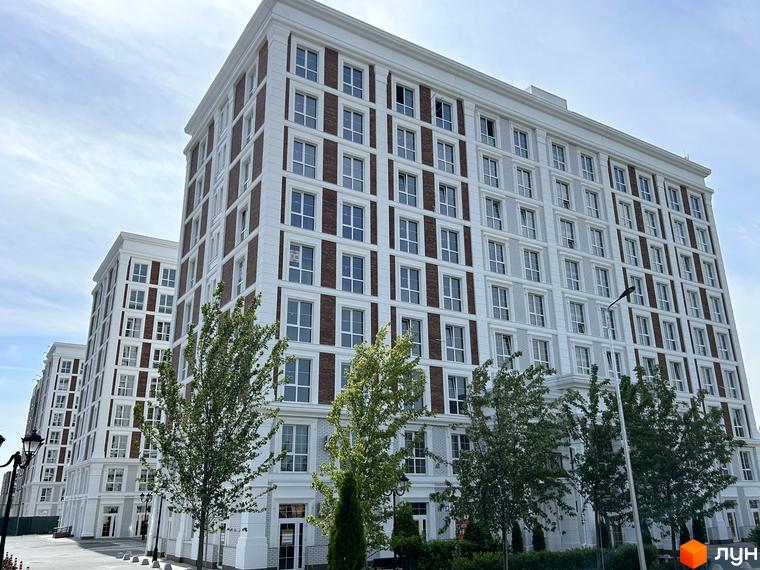 Фасад житлового комплексу OXFORD з цегляними вставками та великою кількістю вікон. Навколо будівлі висаджені дерева.