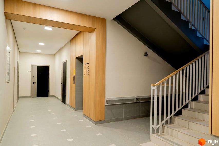 Вхідна група та сходова клітина в новобудові ЖК WAWEL. Коридор з дверима та ліфтом, оздоблені деревом та сірою плиткою.