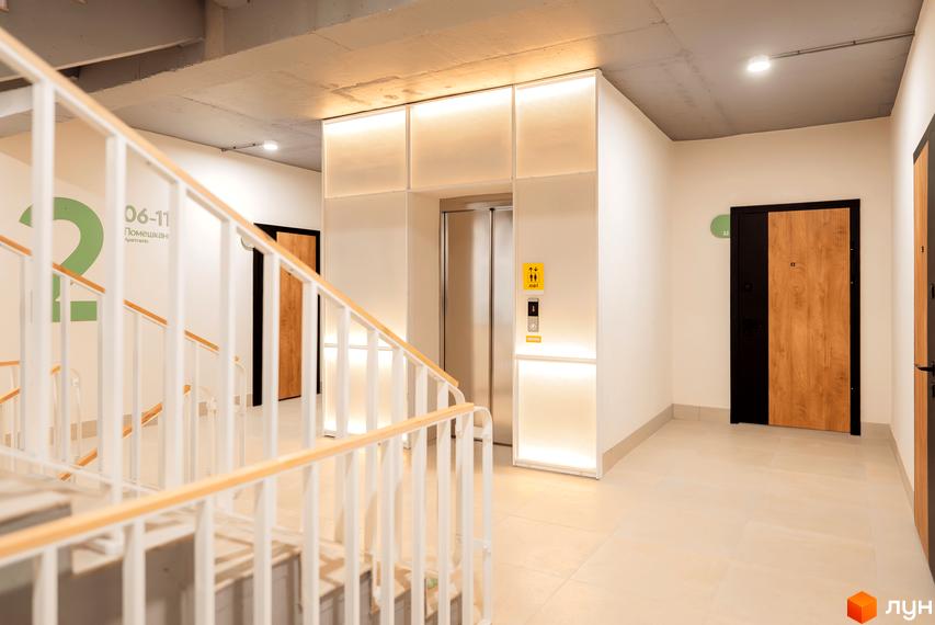 Коридор поверху в Житловому комплексі Долішній з освітленою зоною ліфта, сходами та дерев'яними вхідними дверима.