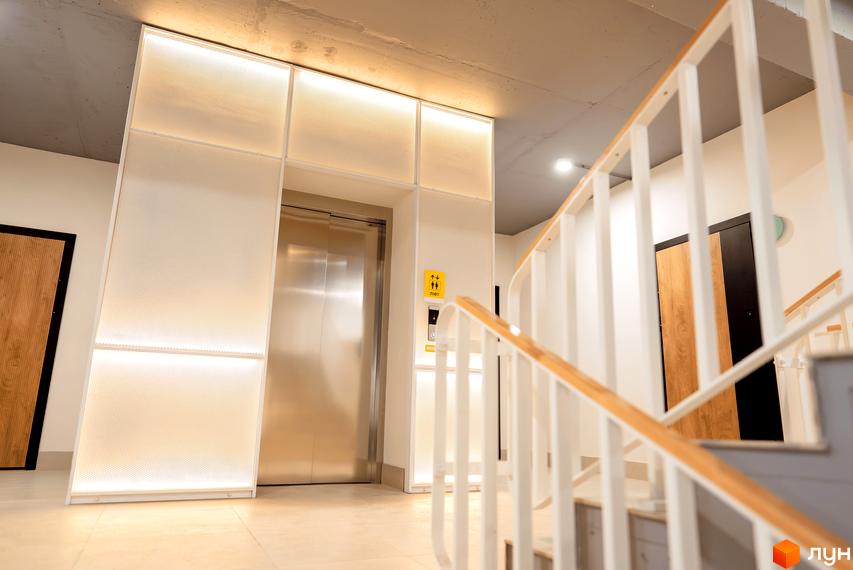 Сучасний вхід у житловий комплекс Долішній з ліфтом та сходами. Оздоблення виконане у світлих тонах з використанням перфорованих панелей та підсвітки.
