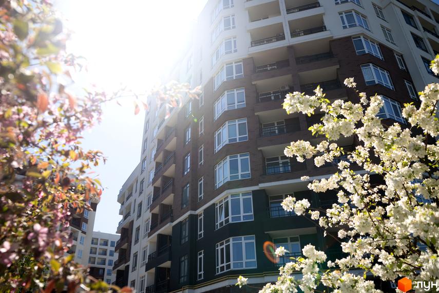 Житловий комплекс Синергія Сіті з фасадами з цегли та білої штукатурки, оточений квітучими деревами.