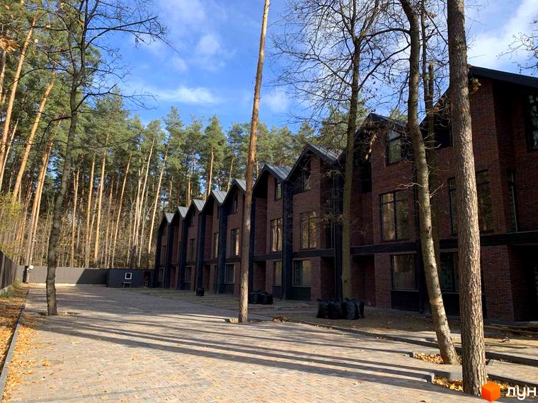 Таунхауси Forest Lane з цегляним фасадом та темними дахами розташовані серед соснового лісу, поруч брукована територія та паркан.