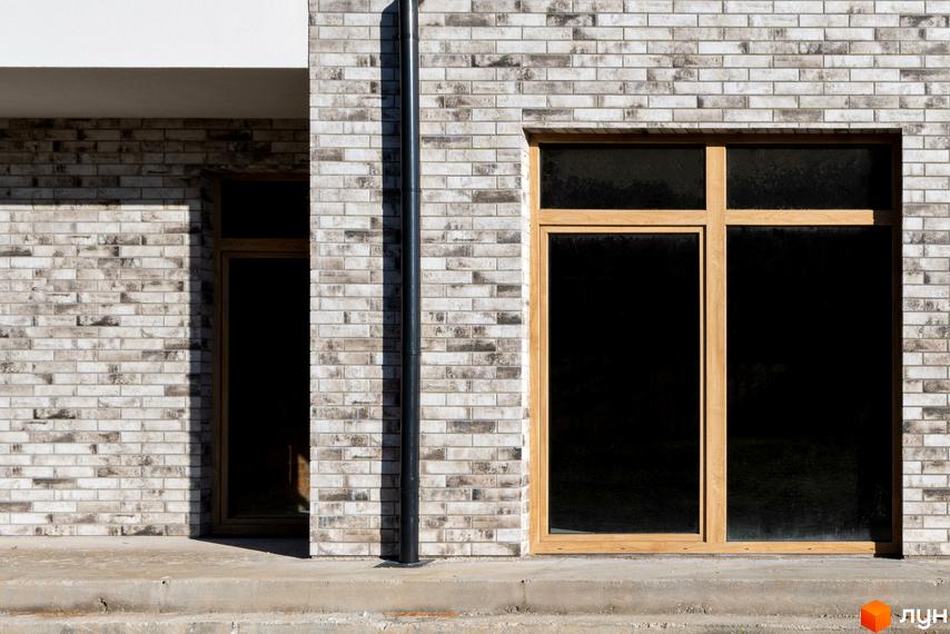 Котеджне містечко LOTUS: фасади з сірої цегли та великі дерев'яні вікна. Біля будинку бетонні сходи та чорна водостічна труба.