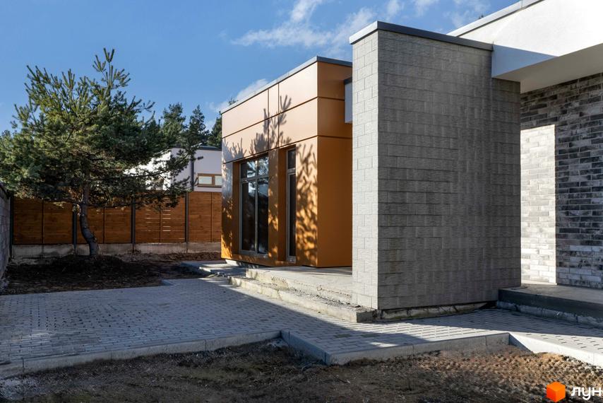 Котеджне містечко LOTUS: будинок з коричневою та сірою облицюванням, вікнами та прибудинковою територією з бруківки та зеленими насадженнями.