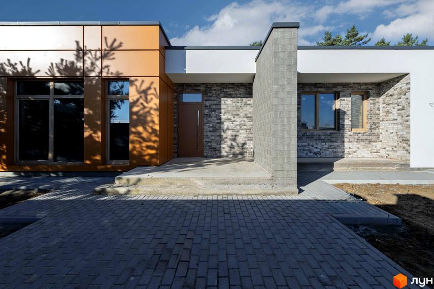 Котеджне містечко LOTUS: фасад будинку з цегляною кладкою та дерев'яними елементами, вимощена бруківкою прибудинкова територія.