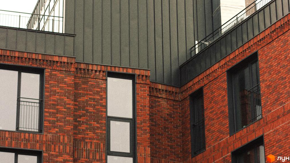 Фасад Житлового комплексу З.40 з червоної цегли, темно-сірого металевого облицювання та вікнами з огорожами.