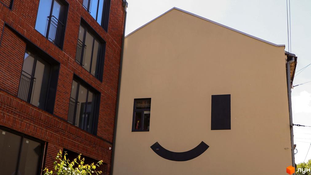 Фасад житлового комплексу З.40 виконаний з червоної цегли, поруч бежева стіна з великим чорним смайликом та вікном.