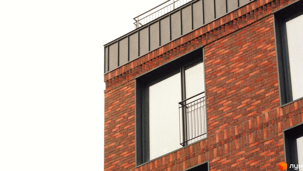 Фасад будинку З.40 виконаний з червоної цегли з характерним візерунком. На зображенні видно великі вікна та балкон з металевими перилами.