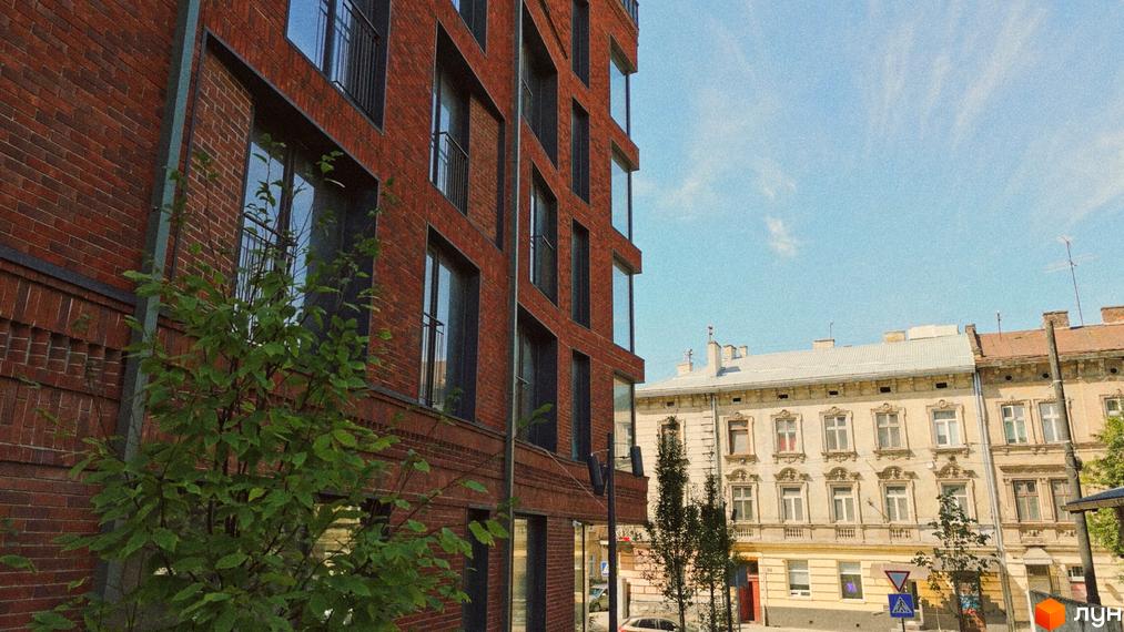 Будівля З.40 з червоної цегли з великими вікнами та балконами, перед нею зелене дерево. Навпроти розташовані старіші будинки та вулиця.