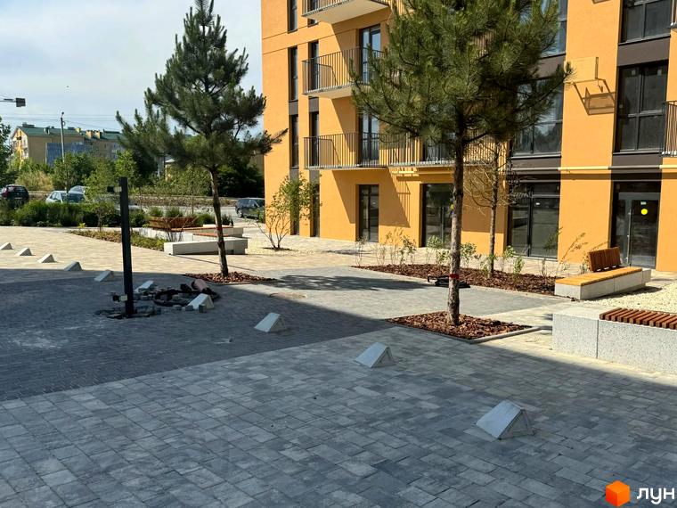 Житловий комплекс Садова Алея: жовта багатоповерхівка з балконами та прибудинкова територія з деревами, лавками та бруківкою.