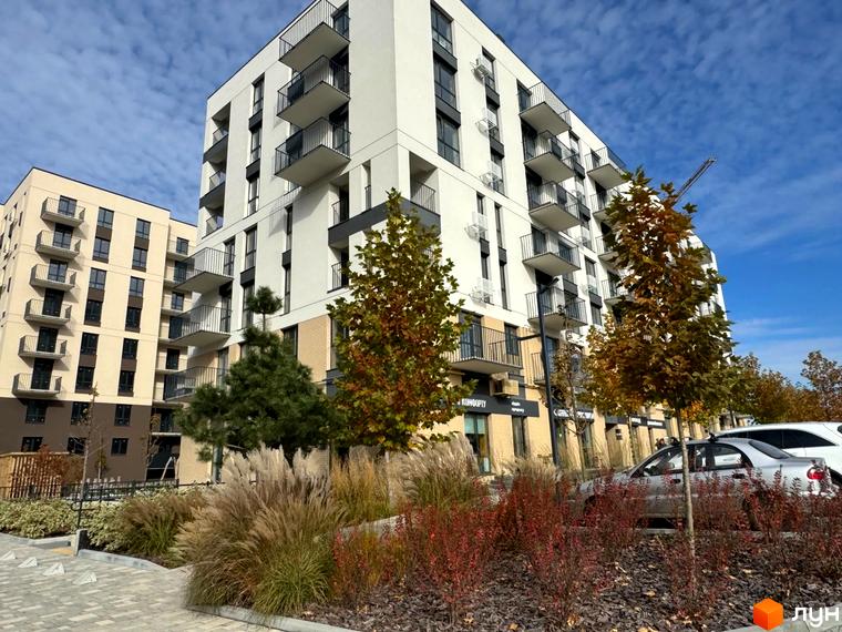 Житловий комплекс Садова Алея: білі та бежеві багатоповерхові будинки з балконами, зелені насадження та дерева навколо.