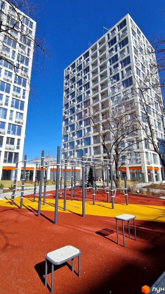 Житловий комплекс Вертикаль: сучасні білі багатоповерхові будинки з балконами та спортивний майданчик з червоним покриттям.