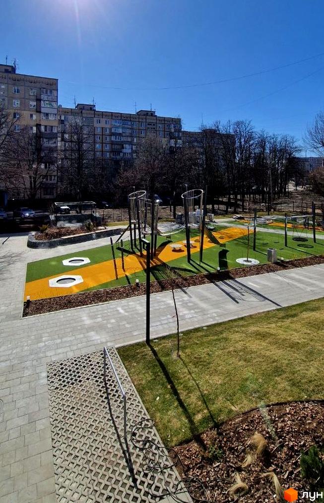 Житловий комплекс Вертикаль: вид на багатоповерхові будинки та сучасний дитячий майданчик з яскравим покриттям та ігровими елементами.