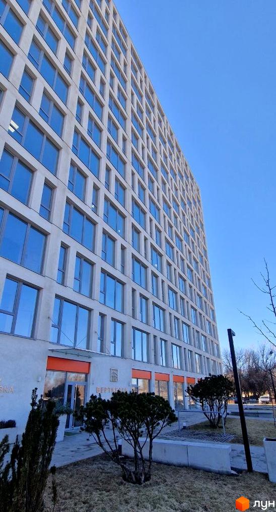 Житловий комплекс Вертикаль - багатоповерхова будівля з численними вікнами та впорядкована прибудинкова територія з деревами та кущами.