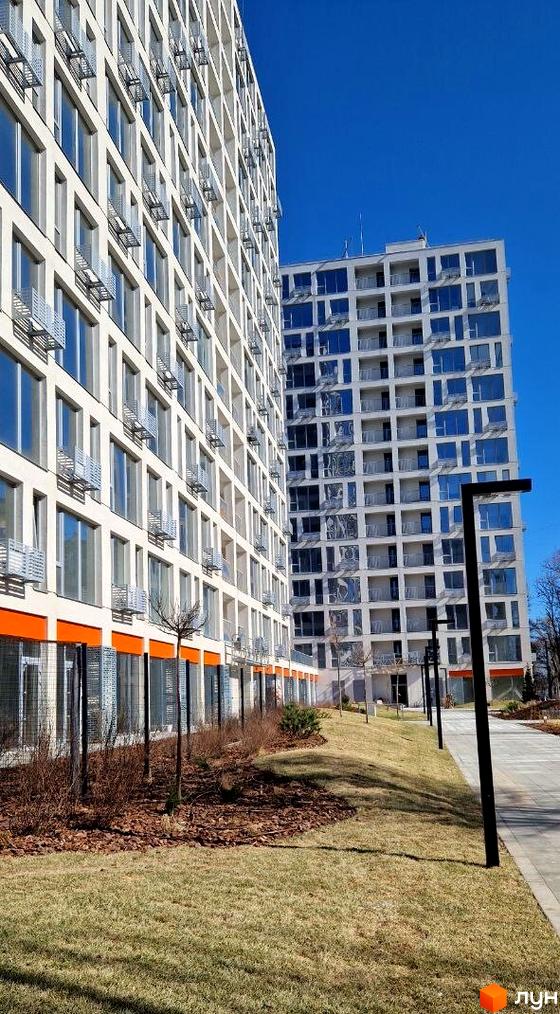 Житловий комплекс Вертикаль - сучасна новобудова з панорамними вікнами та балконами, упорядкована прибудинкова територія з газоном та деревами.