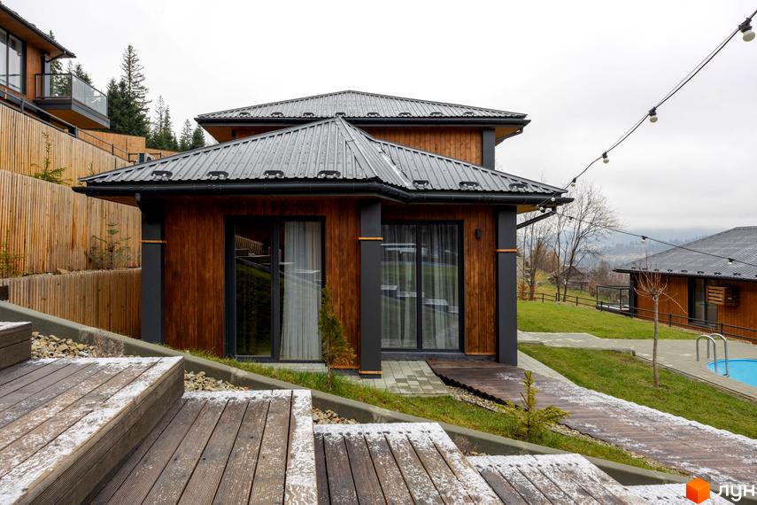 Котеджне містечко Агат Резорт & SPA: дерев'яний будинок з темним дахом, великими вікнами, зеленим газоном та басейном.