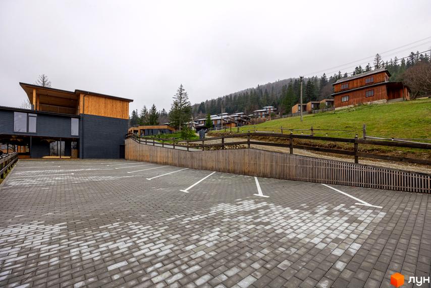 Котеджне містечко Агат Резорт & SPA: будівля з темно-сірим фасадом та дерев'яними елементами, перед якою розташований вимощений паркінг.