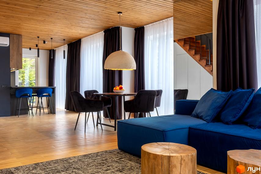 Інтер'єр вітальні з синім диваном, обідньою зоною та кухнею в житловому комплексі КМ Agat Resort & SPA. Дерев'яна стеля та підлога створюють затишну атмосферу.
