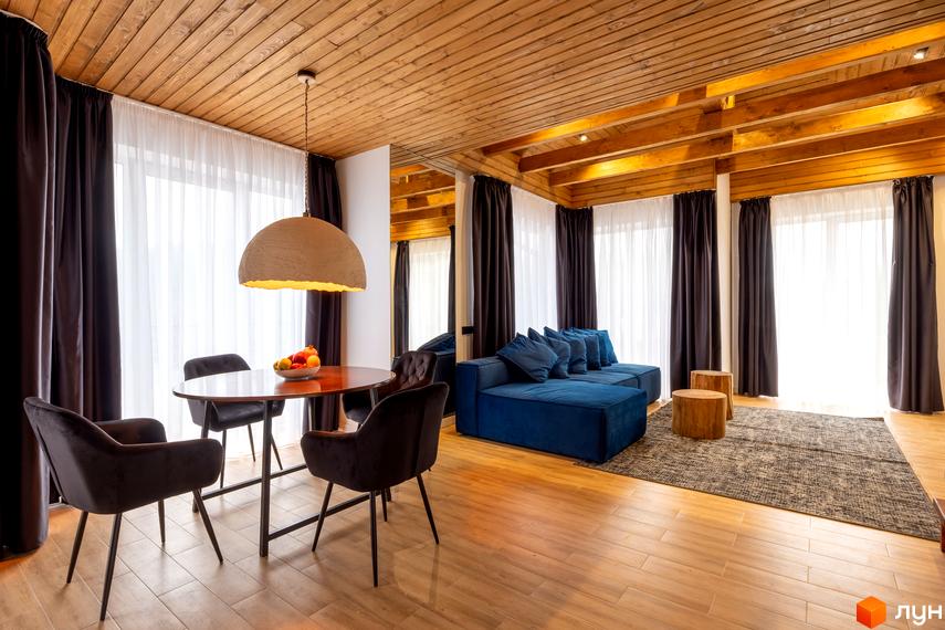 Інтер'єр вітальні Котеджного містечка Агат Резорт & SPA: дерев'яна стеля, великі вікна, синій диван, обідній стіл з чотирма стільцями.