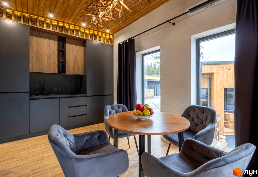 Інтер'єр кухні-вітальні з круглим столом та сірими кріслами. Сучасна кухня з дерев'яними та сірими фасадами.