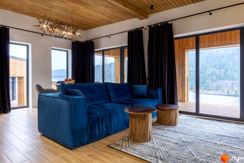 Інтер'єр вітальні з синім диваном та кавовими столиками в КМ Agat Resort & SPA. Вікна виходять на ліс та гори.