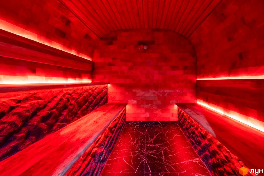 Інтер'єр SPA зони в житловому комплексі КМ Агат Резорт & SPA з червоним підсвічуванням та дерев'яними лавами. Оздоблення стін та підлоги виконано з натуральних матеріалів.