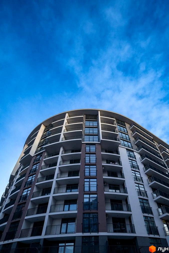 Житловий комплекс Crystal: багатоповерховий будинок з округлим фасадом, численними балконами та великими вікнами, що відображають блакитне небо.