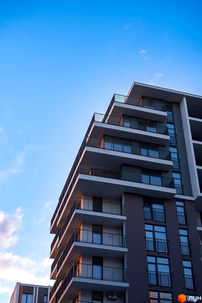 Житловий комплекс Crystal: багатоповерховий будинок з балконами та великими вікнами, фасади темно-сірого кольору з білими елементами на тлі блакитного неба.
